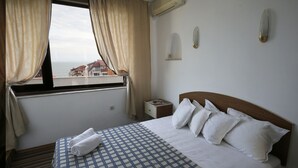Ein Hotelzimmer mit Bett, Nachttisch, Fenster mit Vorhängen und Blick auf Gebäude.