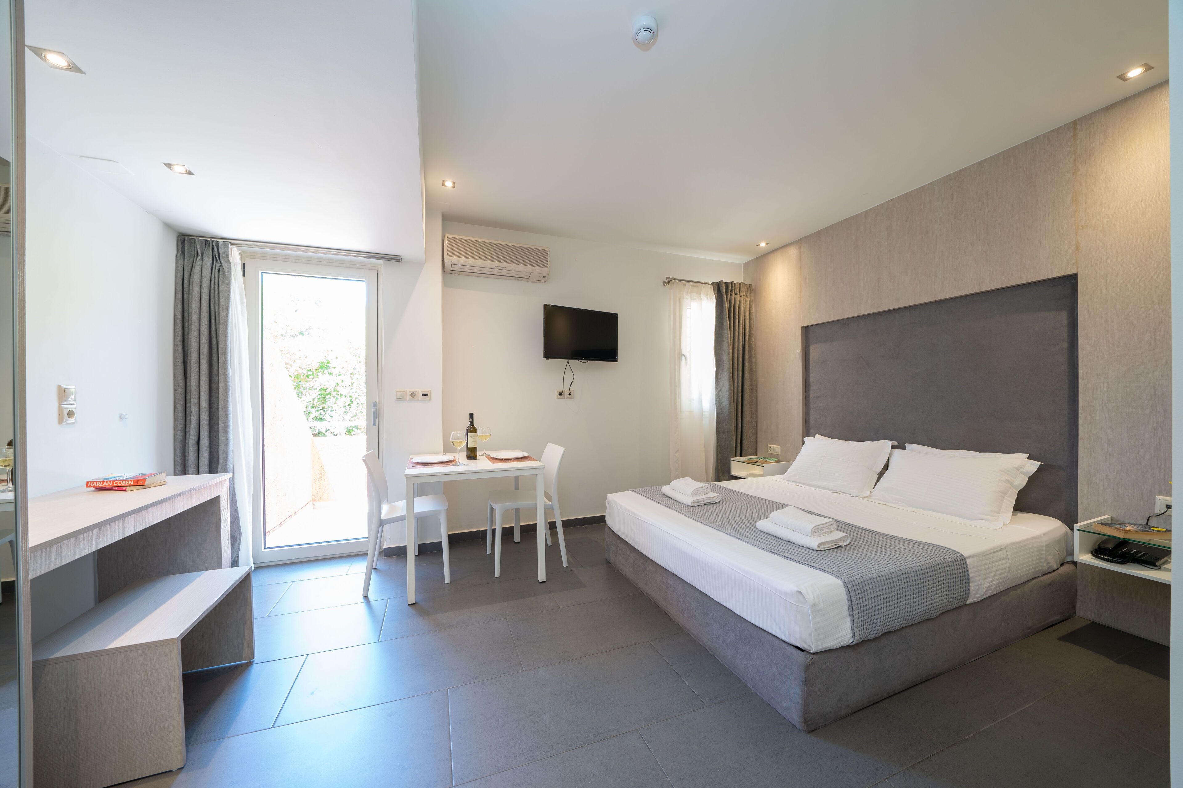 Ein modernes Hotelzimmer mit einem großen Bett, einem Schreibtisch, einem Sessel, einem Fernseher und einem Fenster mit Vorhängen.