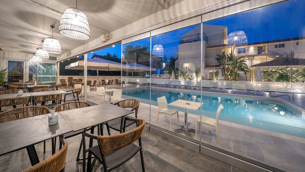 Un espace extérieur avec piscine, des tables et des chaises pour prendre les repas, de grandes fenêtres et une vue sur les bâtiments environnants.