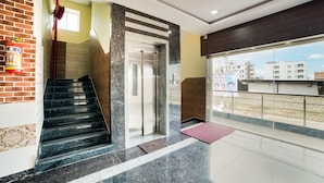 A modern hotel lobby with a marble staircase, a fire extinguisher, a red fire hose, and a view of the outside buildings. - OYO 63209 Hotel Ram Ratan Grand (Hyderabad)