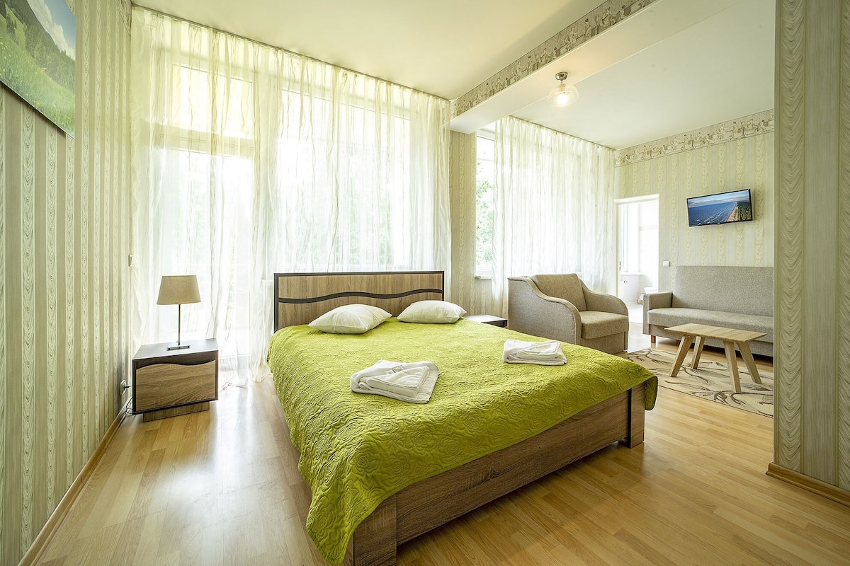 A hotel room with a large bed, two chairs, a small table, and a TV on the wall.