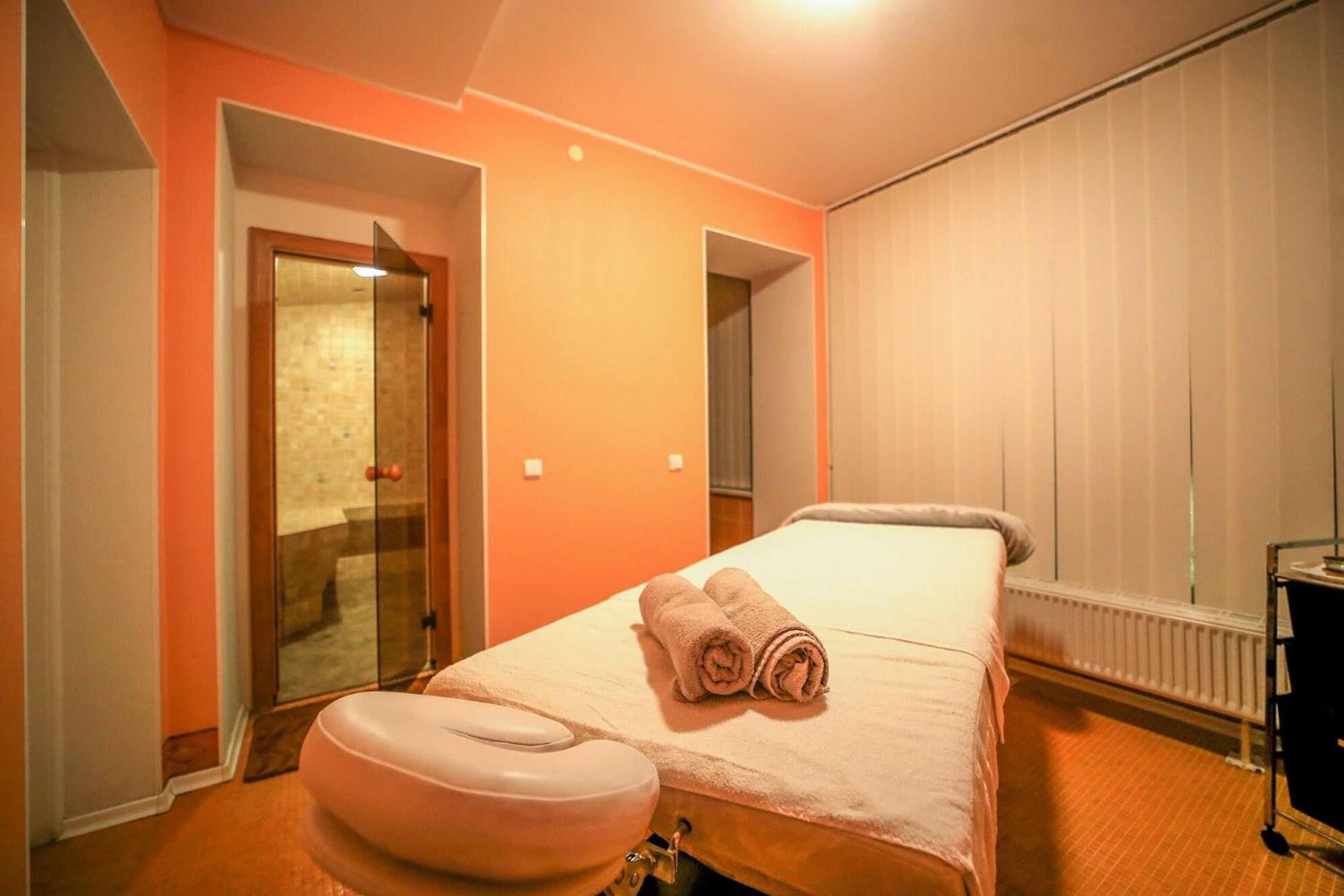 A hotel room with a bed, a massage chair, and a window with blinds.