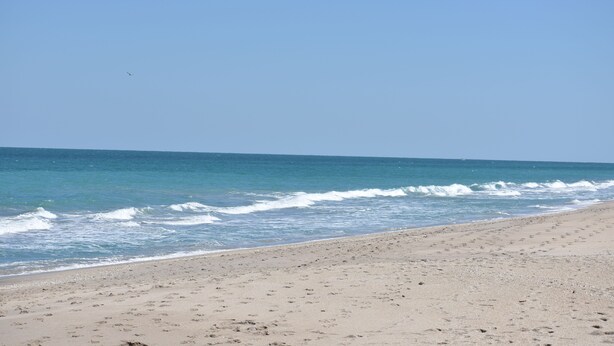 Ein Strand mit blauem Himmel, Wellen und Fußabdrücken im Sand.