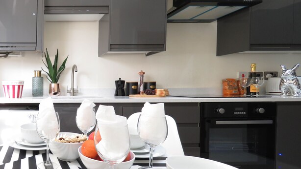 Une cuisine moderne avec des meubles de couleur sombre, une hotte de cuisinière en acier inoxydable et un lave-vaisselle.