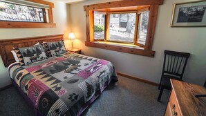 Um quarto com cama, mesa de cabeceira, cadeira, janela com persianas e ventilador de teto.