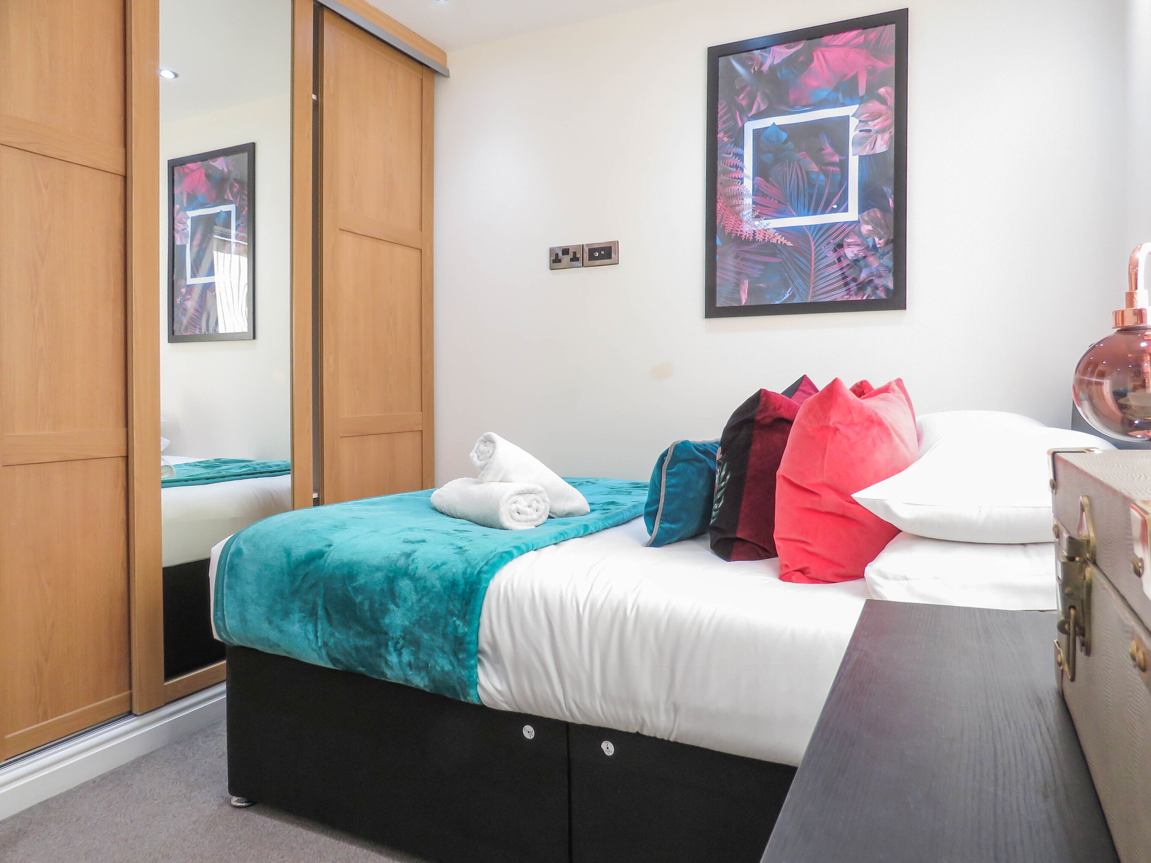 A bedroom with a bed, a wardrobe, a mirror, and a framed picture on the wall.