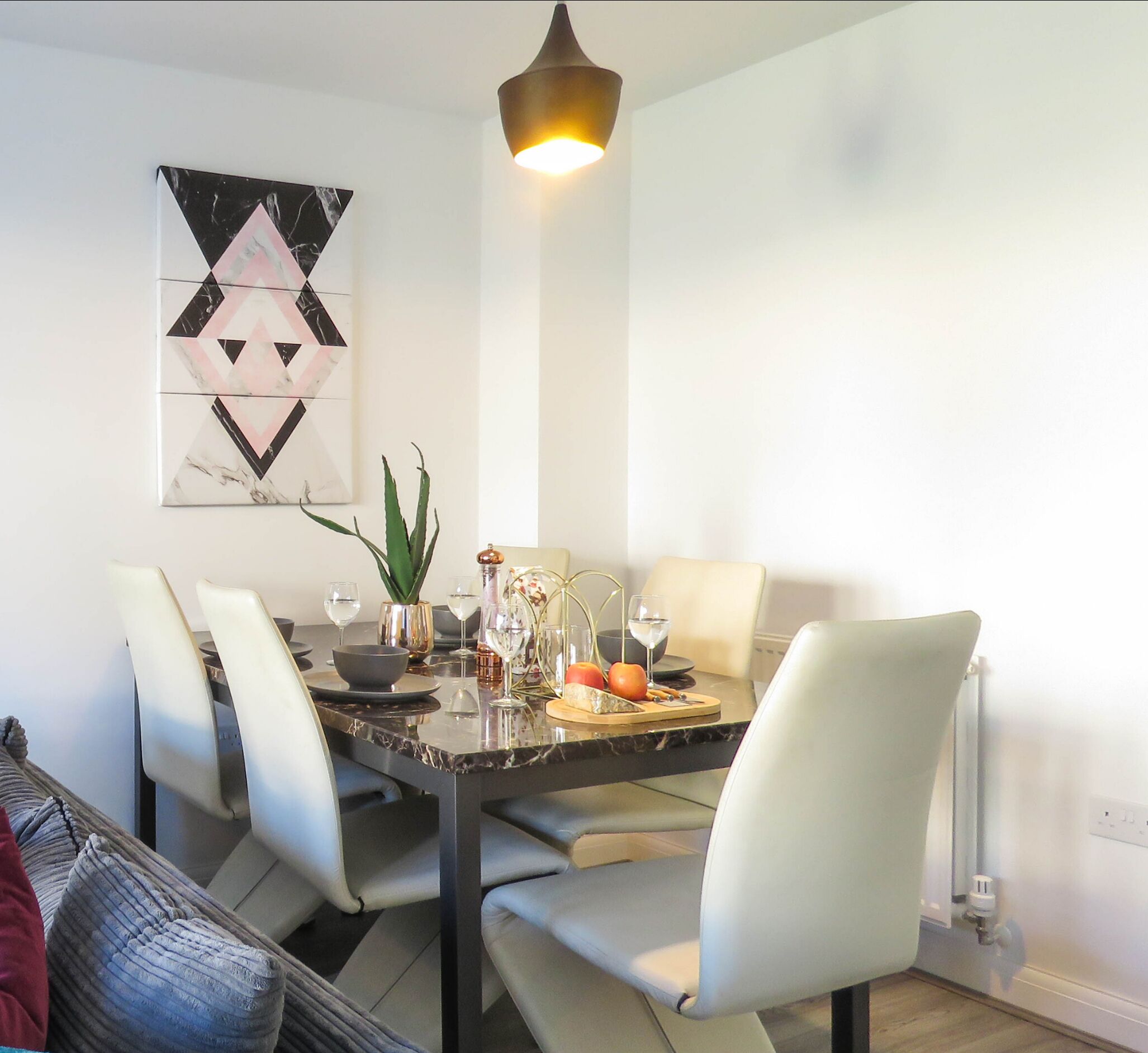 A dining area with a marble table, white chairs, a modern pendant light, and a geometric wall art piece.