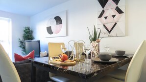 Un comedor con una mesa de mármol, cuatro sillas, un televisor y una planta.