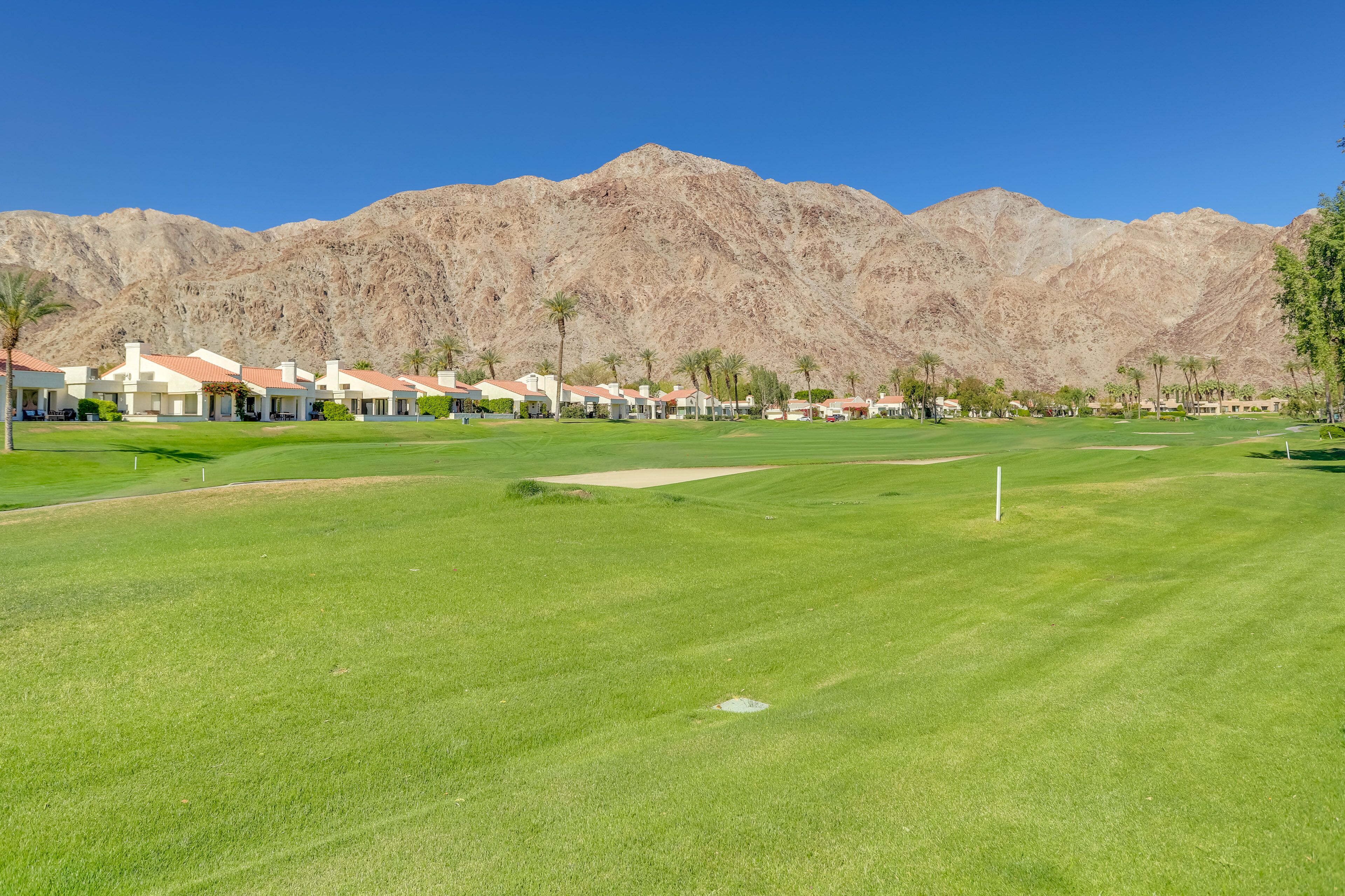 A golf course with a mountain backdrop, well-maintained grass, and a clear sky.