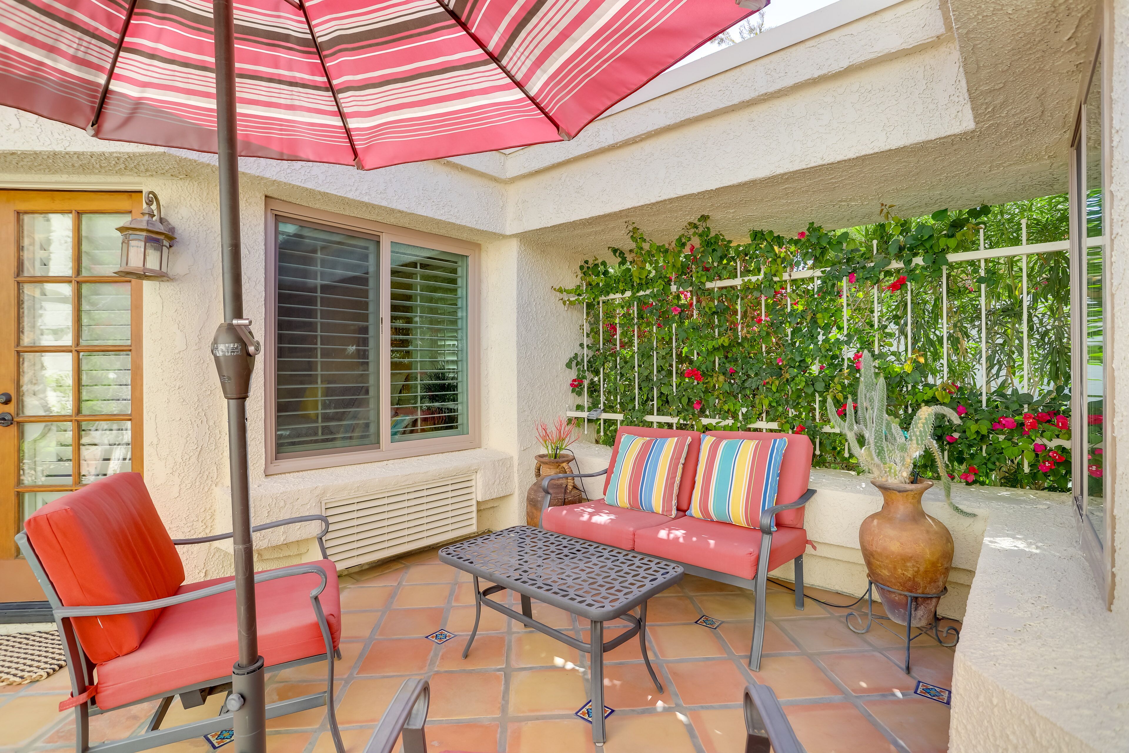Une terrasse avec un canapé rouge, une table en métal et un parasol à rayures.