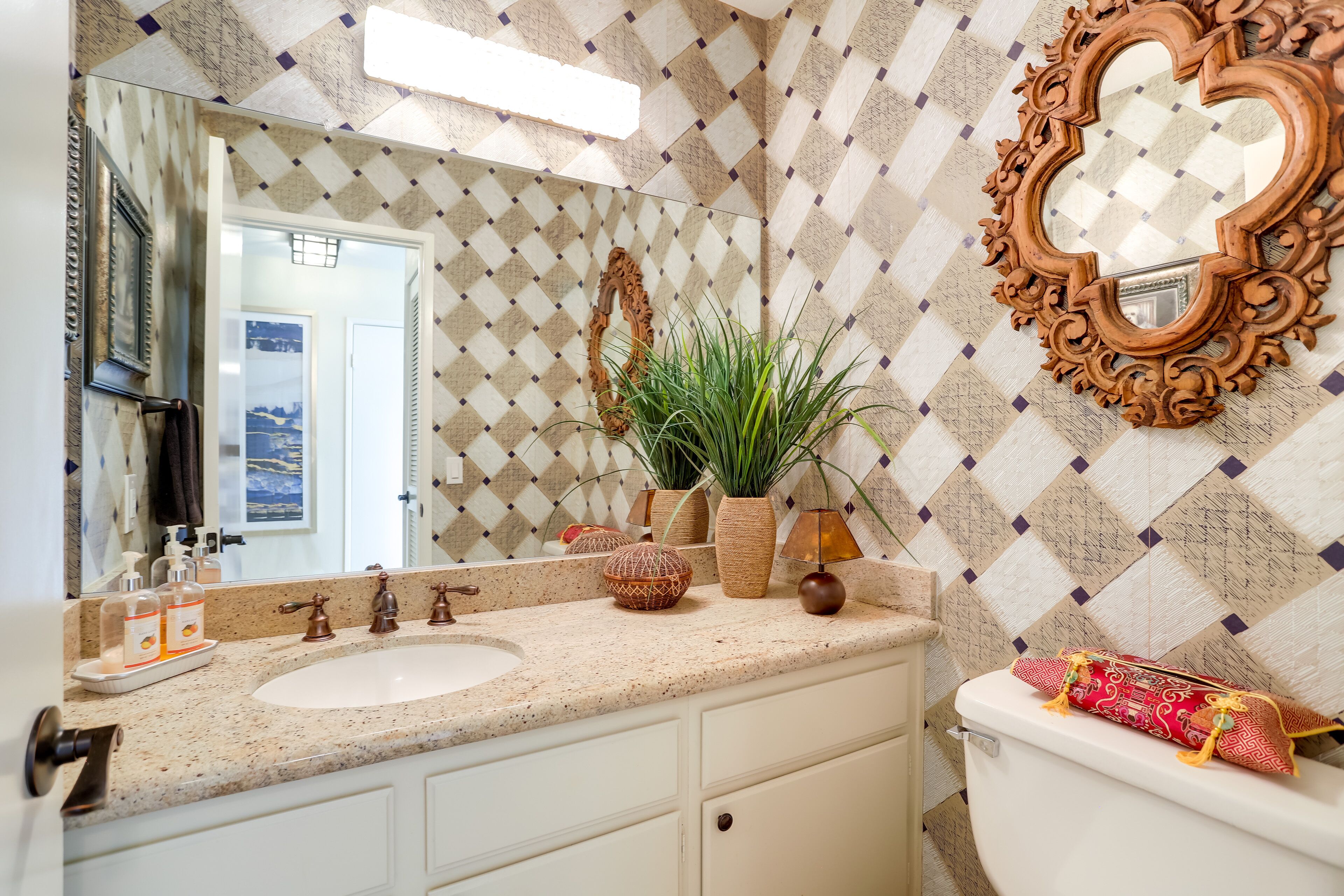 A bathroom with a diamond-patterned wall, a round mirror, a sink, and a toilet.