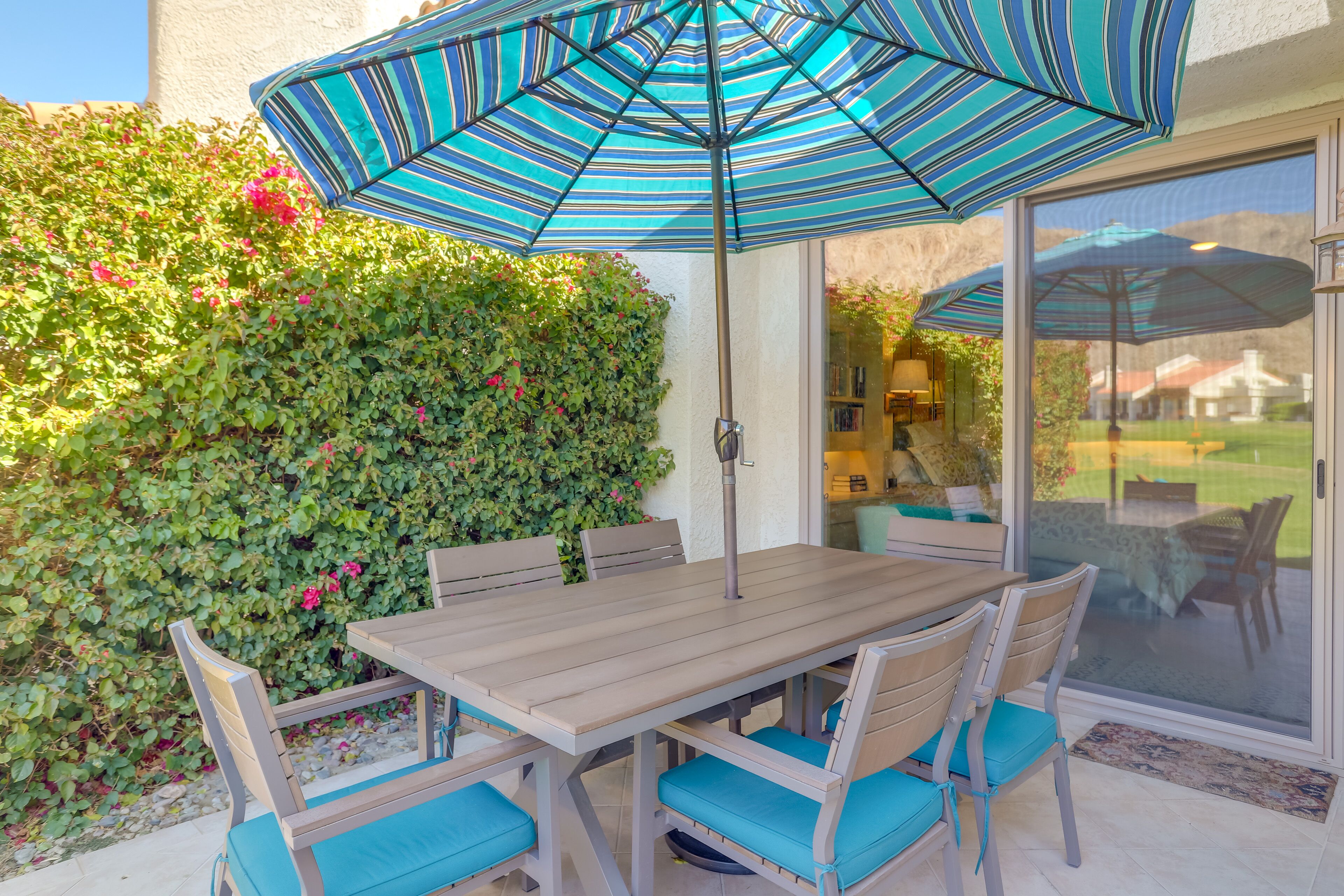 Eine Terrasse mit Tisch und Stühlen, einem gestreiften Sonnenschirm und einer Glasdoor, die zu einem Garten führt.