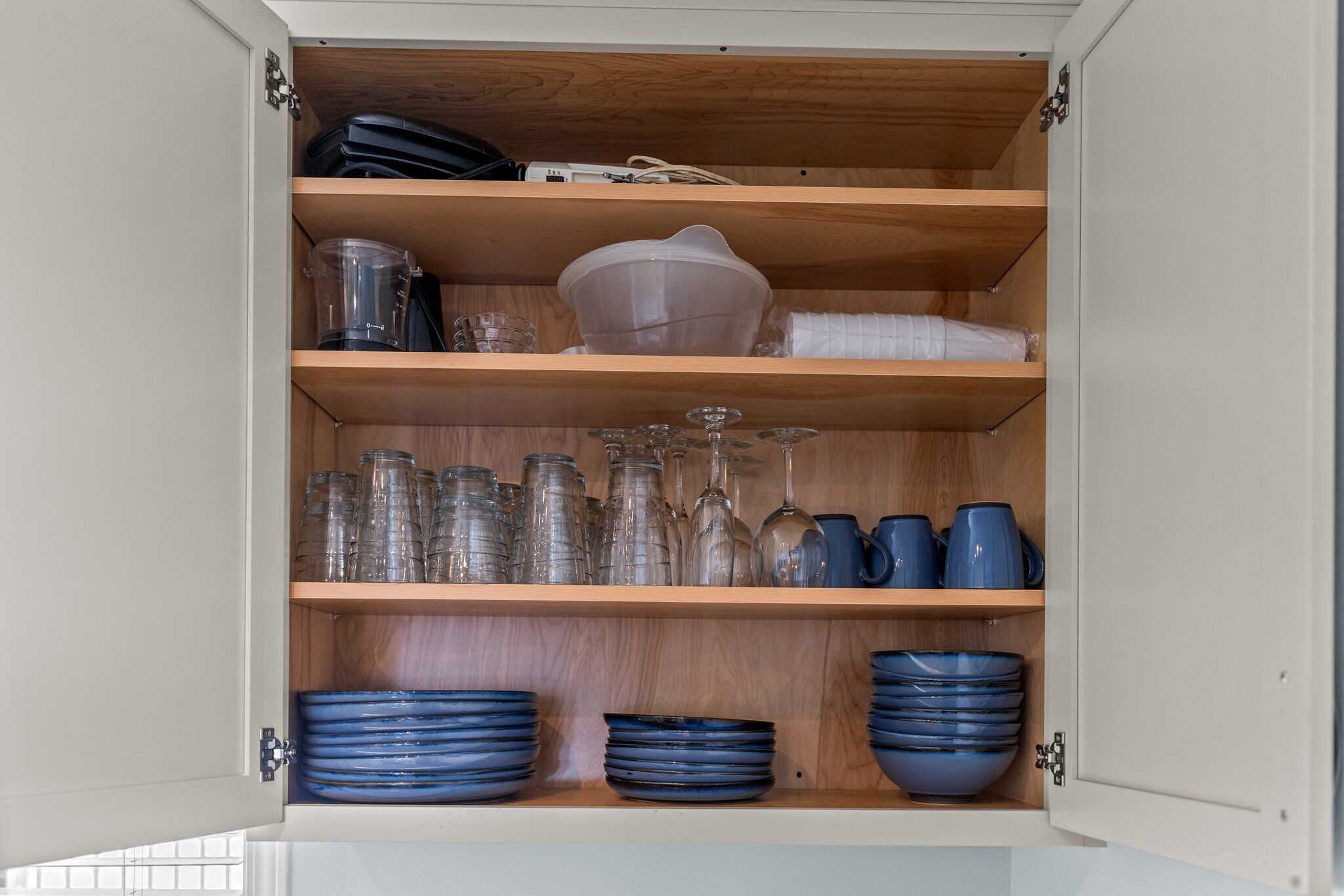 A kitchen cabinet with shelves containing glassware, plates, and a blender.
