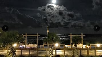 Une vue nocturne d’une plage avec une jetée en bois, des palmiers et une structure en forme de croix.