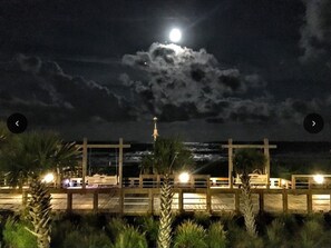 Vista nocturna d'una platja amb un moll de fusta, palmeres i una estructura en forma de creu.