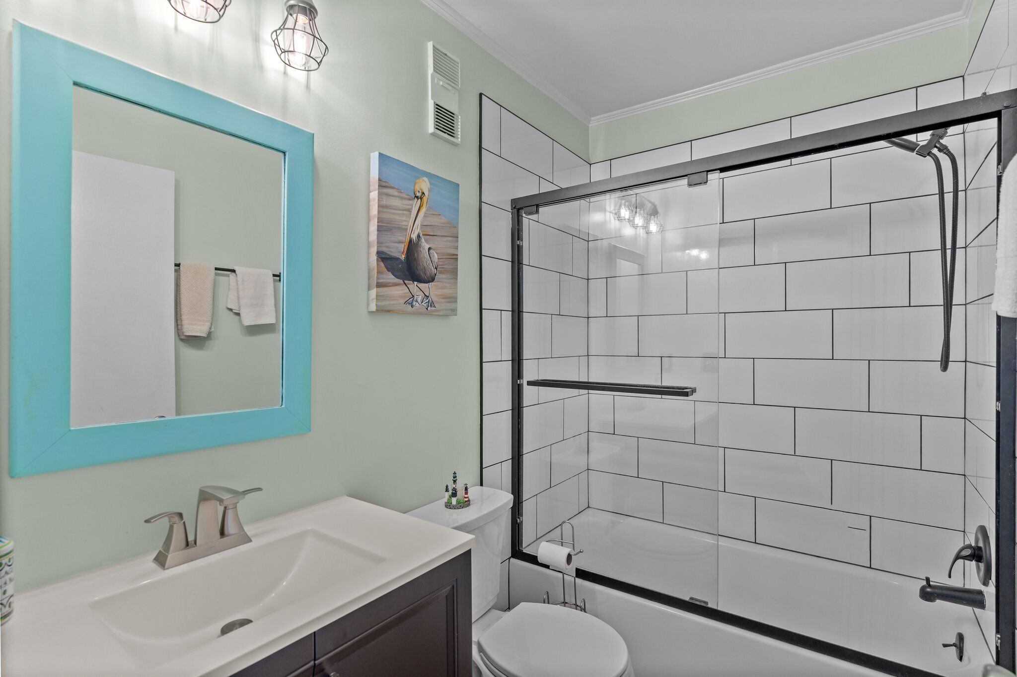 A bathroom with a white sink, a mirror with a blue frame, a toilet, and a shower area with white tiles.