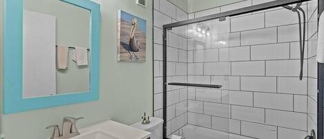 A bathroom with a white sink, a mirror with a blue frame, a toilet, and a shower area with white tiles.
