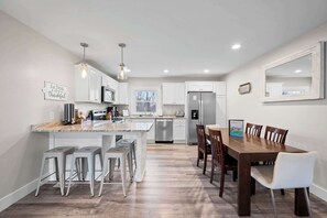 A modern kitchen with white cabinets, stainless steel appliances, and a wooden dining table with bar stools.