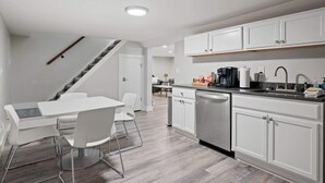 Een moderne keuken met witte kastjes, een inbouw vaatwasser en een eethoek met een witte tafel en stoelen.