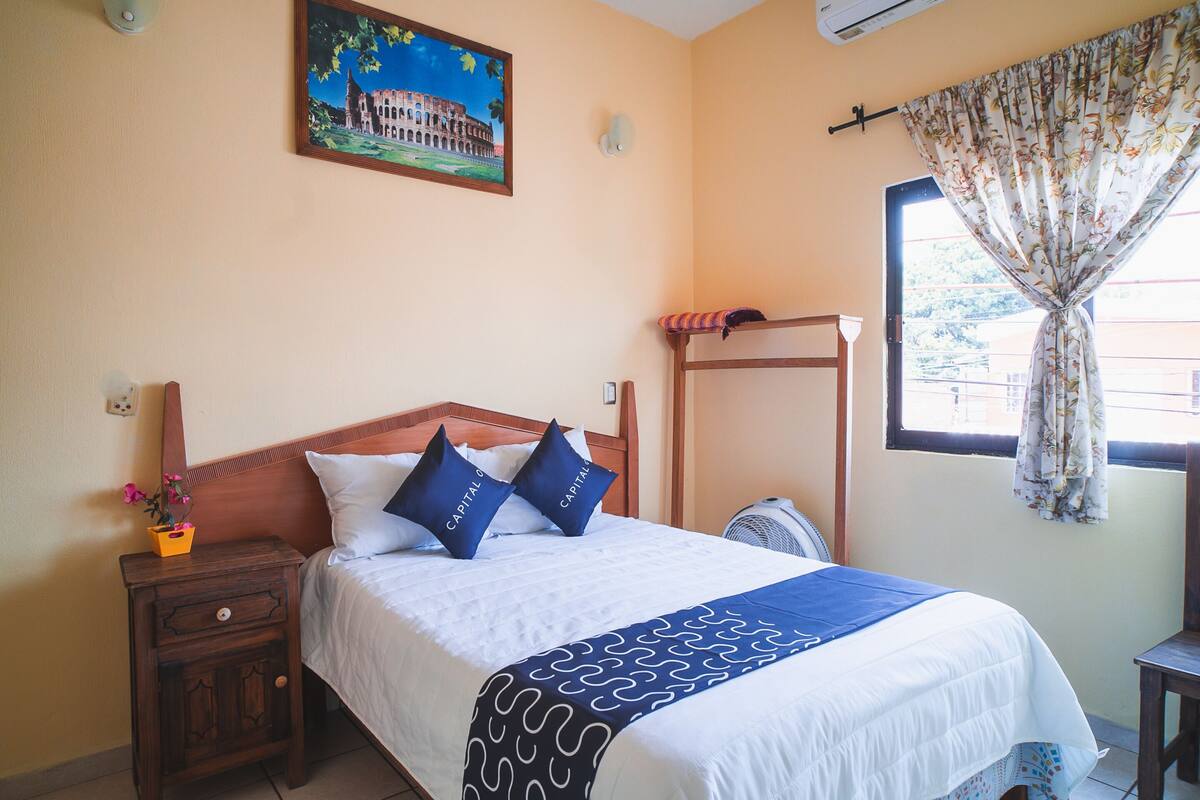 A neatly made bed with a patterned bedspread, a wooden headboard, and two pillows with text.