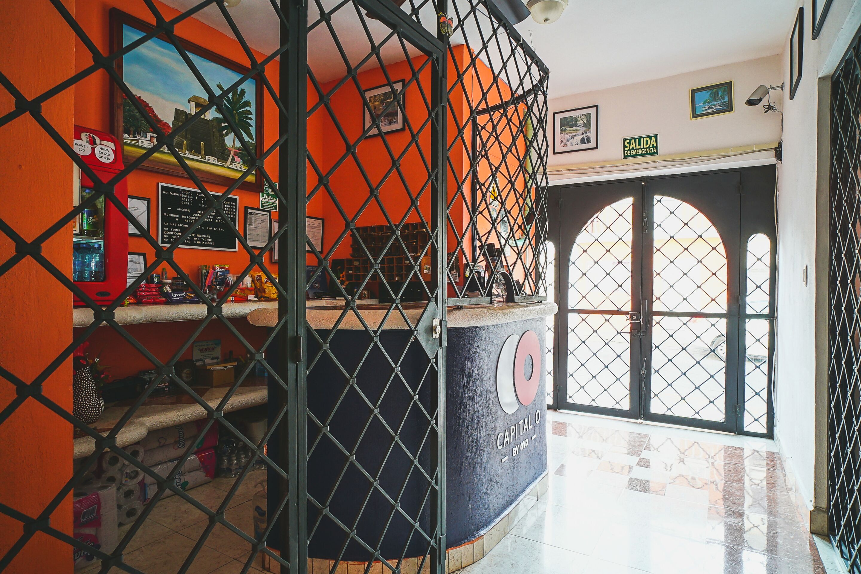 Una zona de recepció amb mostrador, un senyal que indica la sortida i una vista a través d'una porta de vidre.