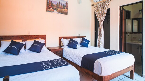 A hotel room with two beds, a painting on the wall, an air conditioning unit, and a bathroom visible through an open door. - Capital O Hotel Aurora, Tuxtla Gutiérrez (Tuxtla Gutierrez)