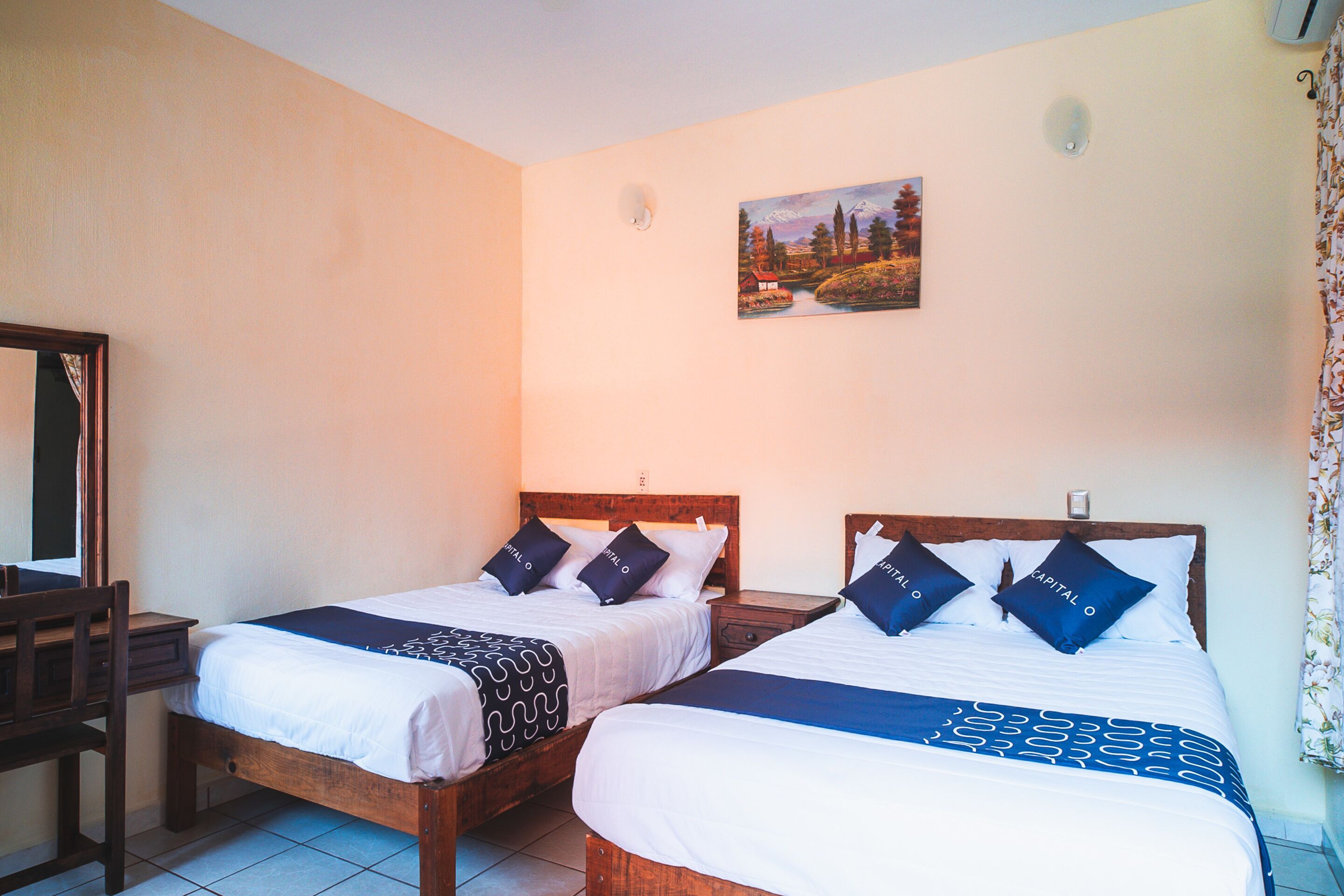 Dos camas individuales con estructura de madera, ropa de cama blanca y almohadas azul oscuro.