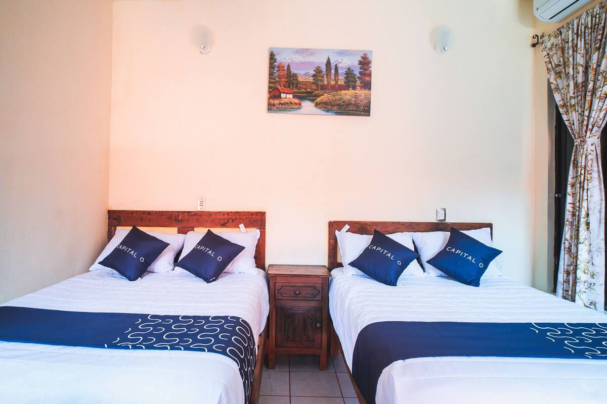 A hotel room with two beds, each with matching headboards and pillows labeled "Capital O".