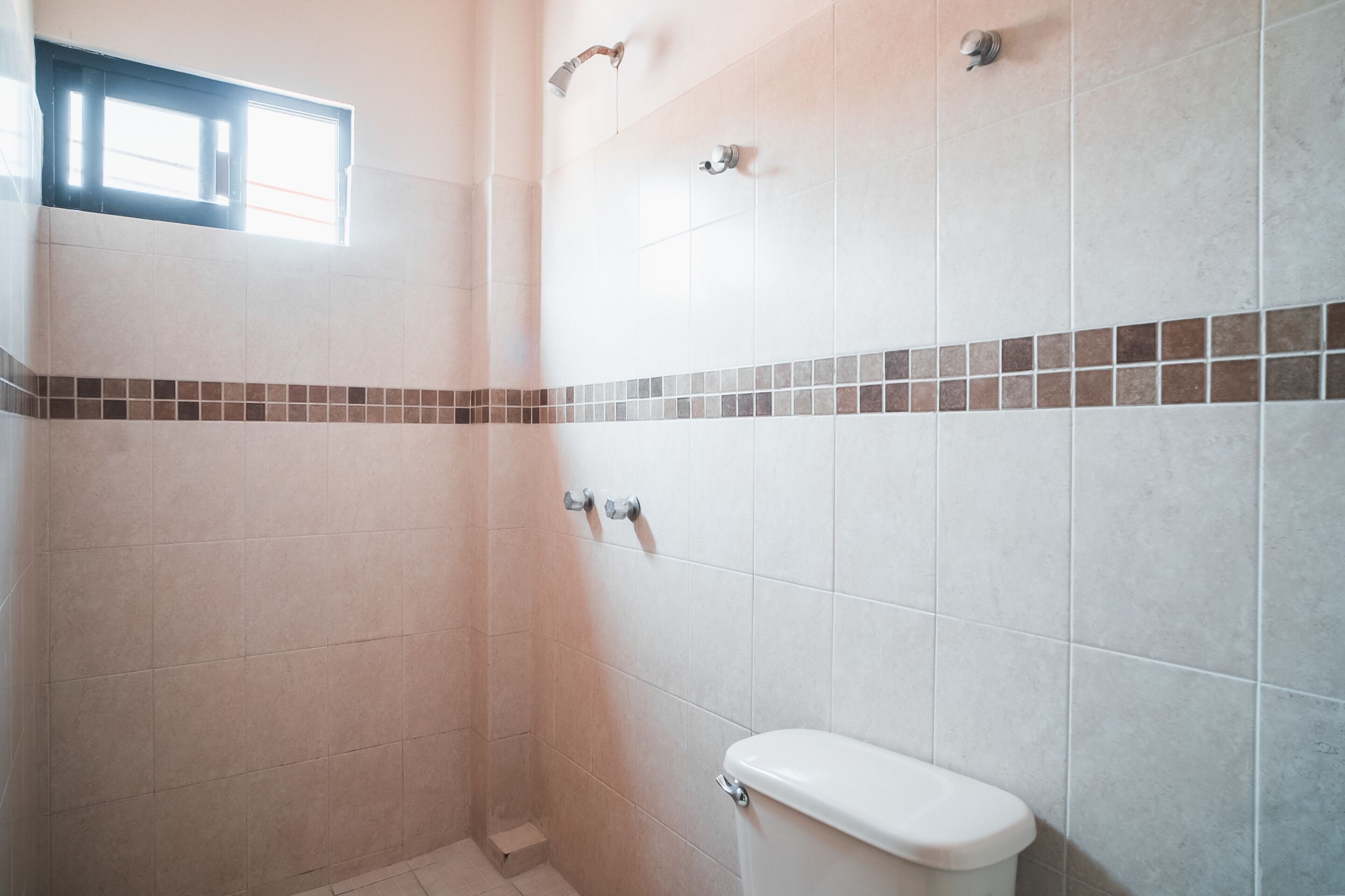 Ein Badezimmer mit Dusche, Toilette und Fenster.