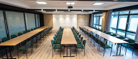 A conference room with long tables and chairs, large windows, and a projector on the ceiling.