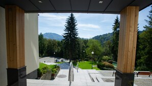 Une vue depuis un espace abrité, avec un escalier en pierre menant à une route, le tout entouré de verdure et avec une montagne en arrière-plan.
