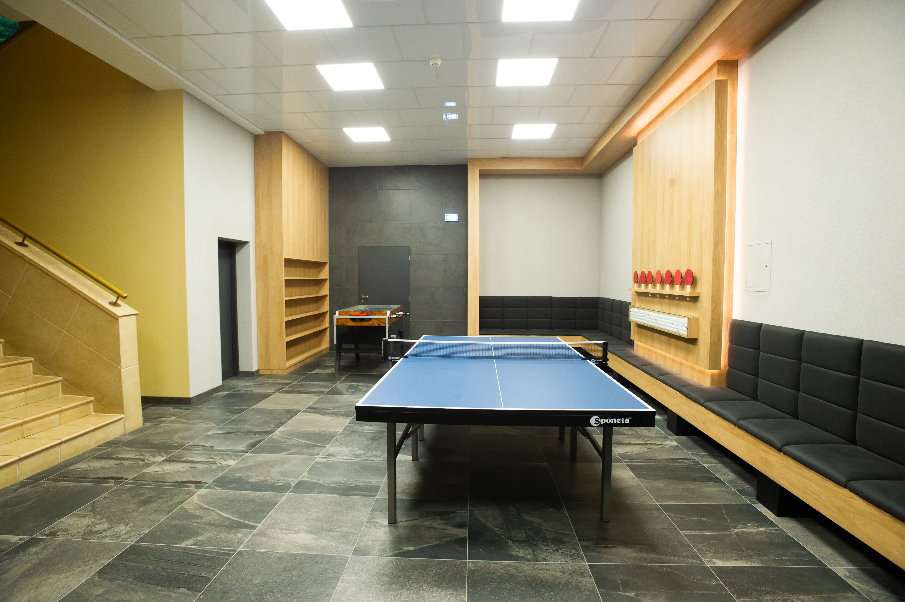 Une table de ping-pong dans une pièce qui comprend un escalier, un comptoir d’accueil et un espace détente.
