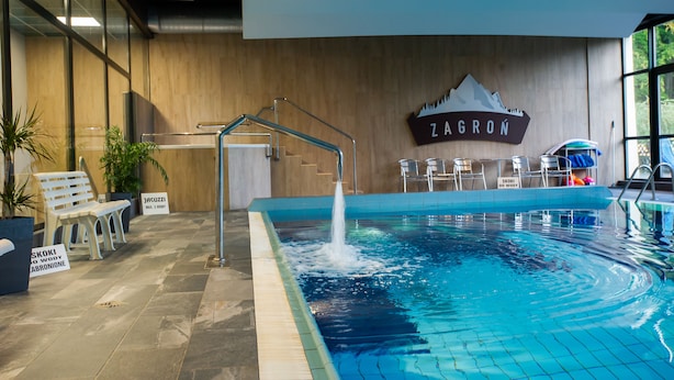 Une piscine intérieure dotée d’une fontaine, d’un espace détente et d’un panneau indiquant « ZAGRON ».