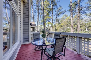 A covered outdoor deck with a glass-top table and two chairs, surrounded by a wooden deck and a white fence. - 7653 Huntington - Beautiful Lagoon Views/Screened in Porch (Hilton Head Island)
