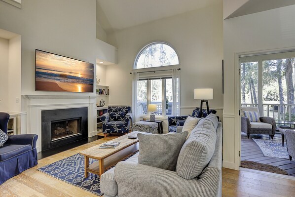 A spacious living room with a fireplace, a large window, and a view of the outdoors. - 7653 Huntington - Beautiful Lagoon Views/Screened in Porch (Hilton Head Island)