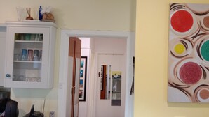 Een kamer met een witte kast met glaswerk, een schilderij met abstracte cirkels en een deur die naar een andere kamer leidt.