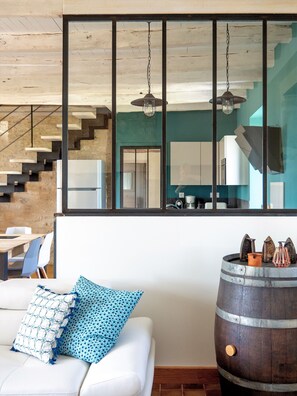 A modern living room with a white sofa, a wooden barrel, and a staircase.