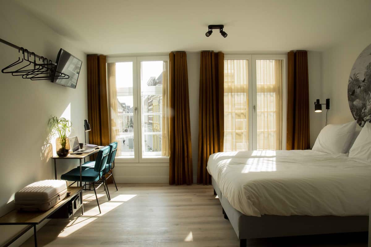 Habitación de hotel con cama, escritorio, silla y ventana con cortinas.