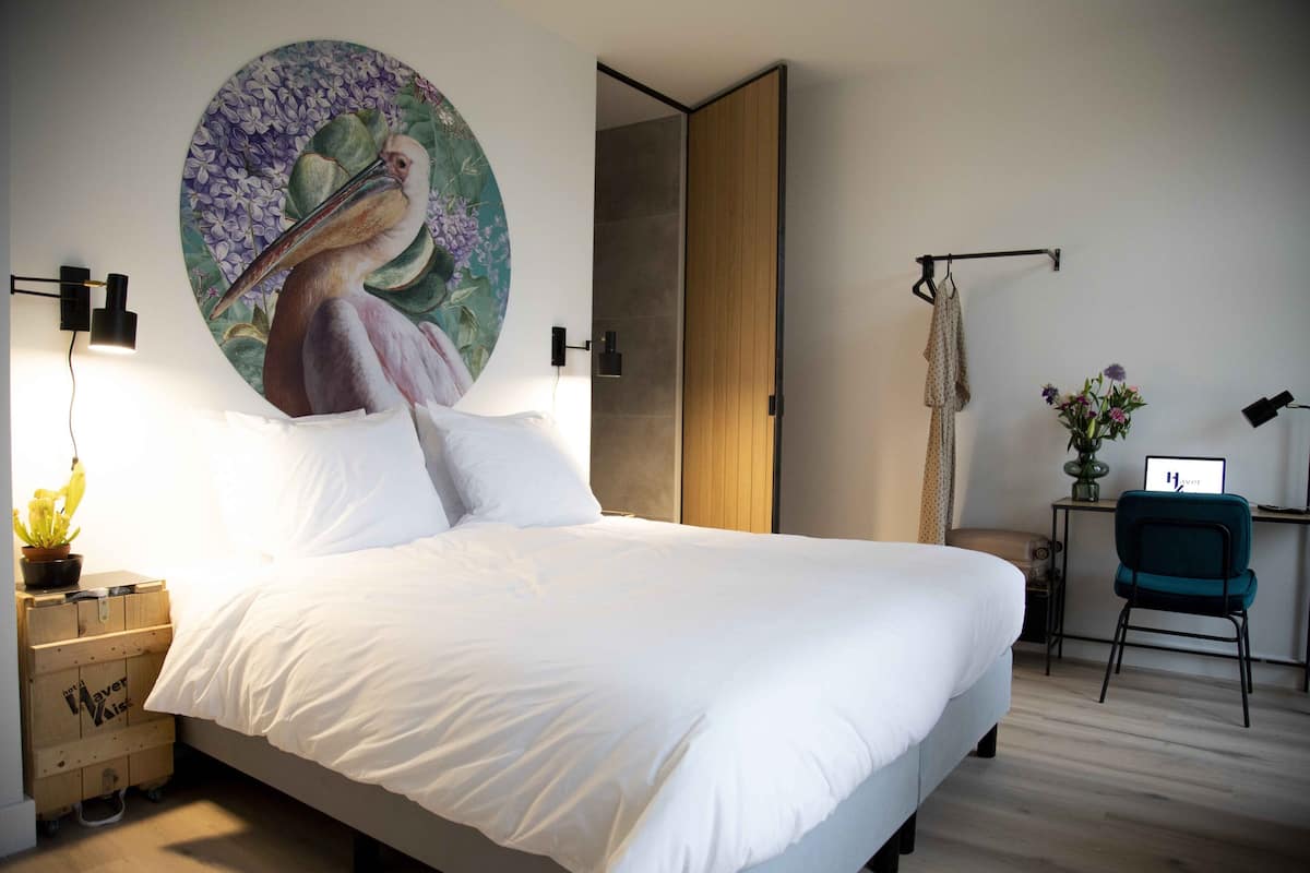 Un dormitorio moderno con una cama grande, un cuadro colgado en la pared, un escritorio con una silla y una pequeña mesa con una planta.