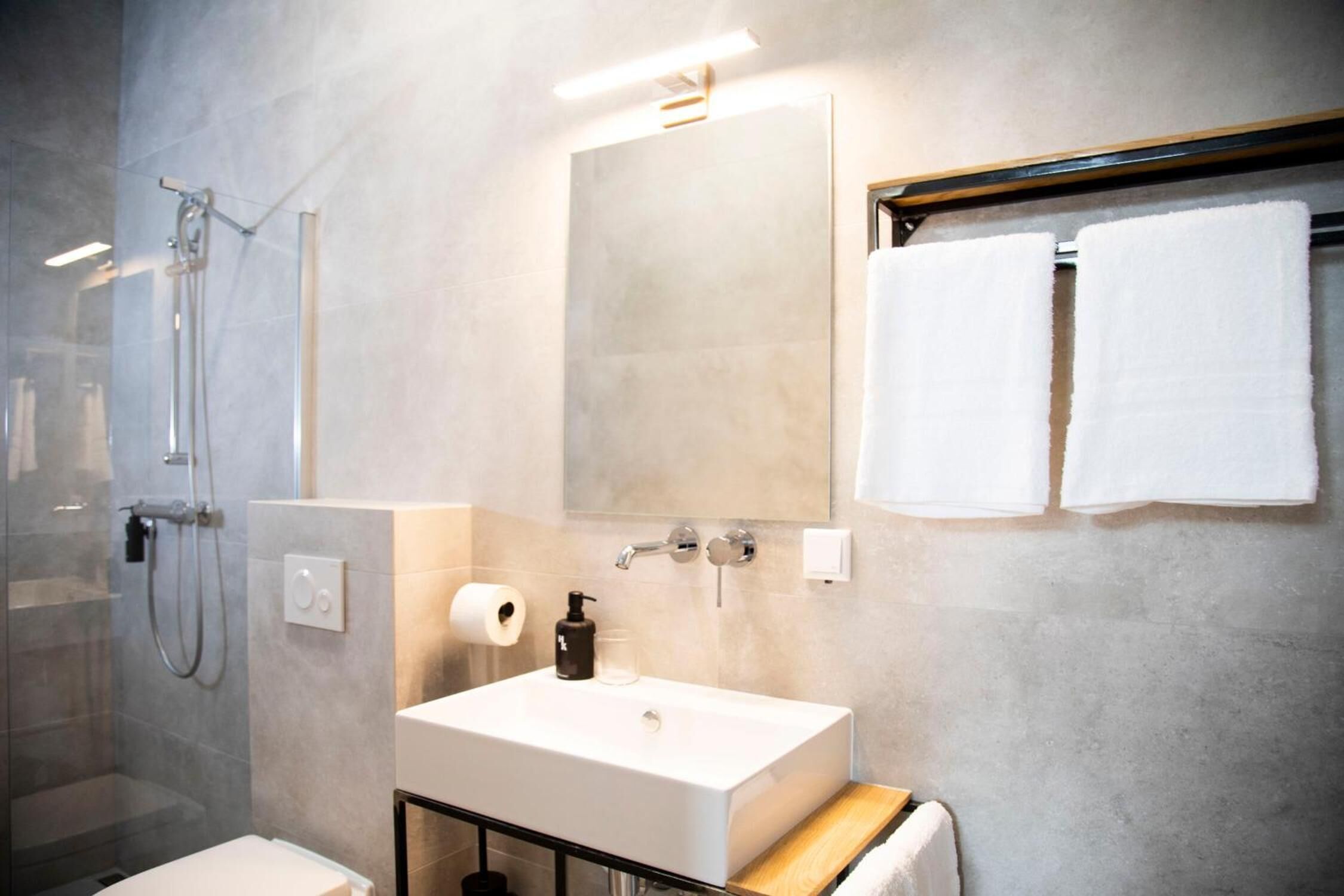A modern bathroom with a glass-enclosed shower, a white sink with a soap dispenser, and two white towels hanging on a towel rack.