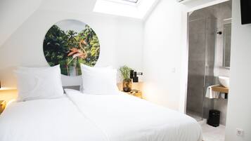 A modern hotel room with a skylight, a bed with white linens, a round wall decoration, a shower area, and a small plant on the nightstand.
