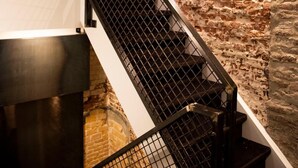 A staircase with a metal railing leading to a lower level, adjacent to a stone wall. - Hotel Haverkist ('s-Hertogenbosch)