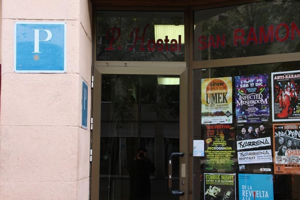 The entrance of P. Hostal San Ramon with a visible parking sign and various event posters on the glass door.