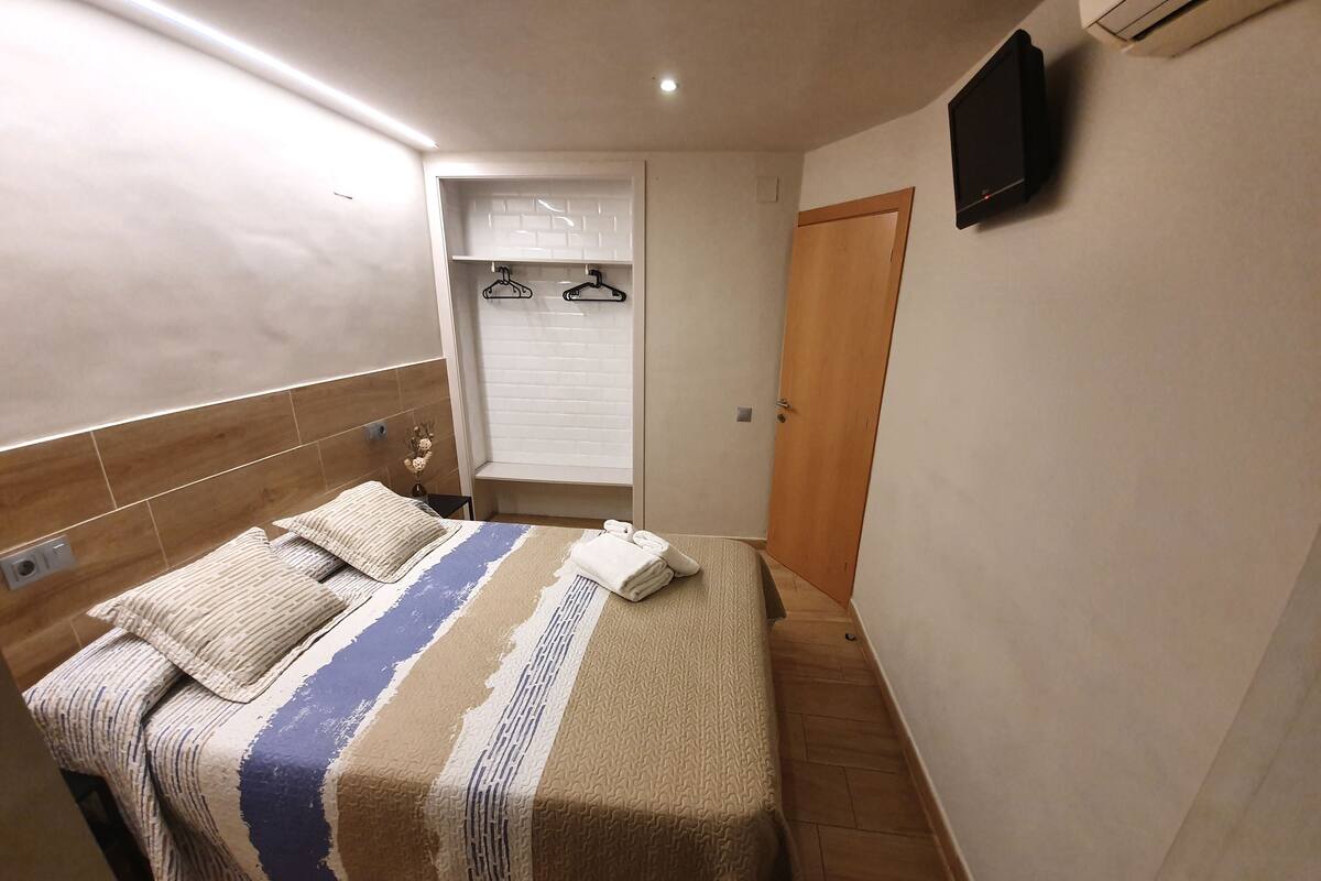 A bedroom with a bed, a wooden headboard, a bedside table, a wall-mounted TV, and a wardrobe with a mirror.