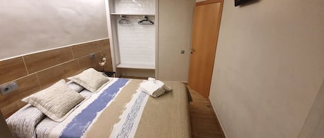 Un dormitorio con cama, cabecera de madera, mesita de noche, televisor montado en la pared y armario con espejo.