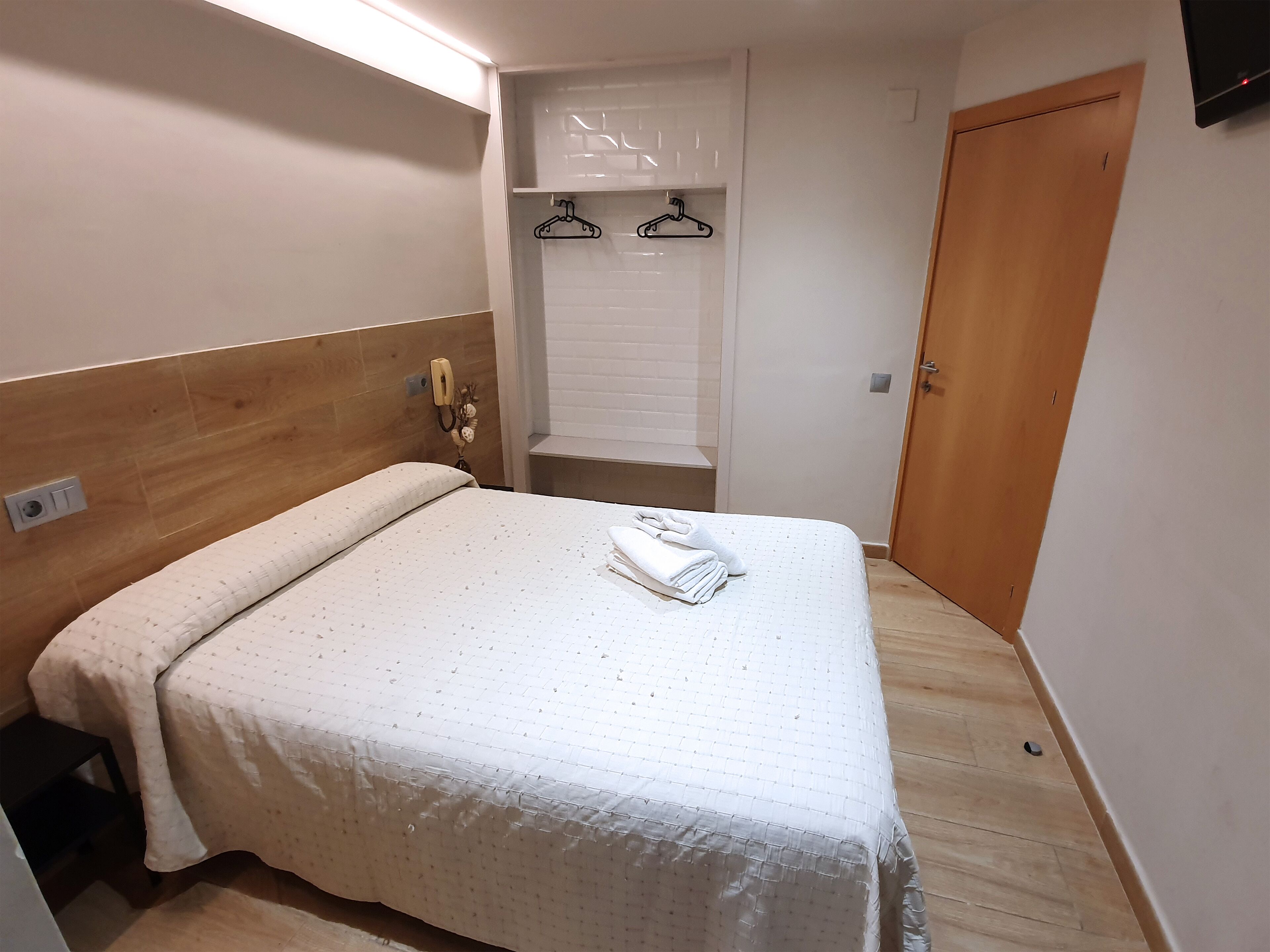 A neatly made bed with a white duvet, a wooden headboard, a bedside telephone, and a wall-mounted towel rack.