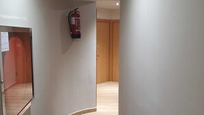 A narrow hallway with wooden flooring, white walls, and a fire extinguisher mounted on the wall. - Hostal Sant Ramón (Barcelona)