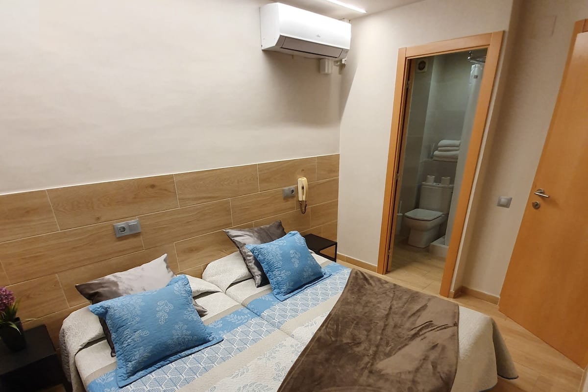 A hotel room with a bed, bedside table, and a bathroom visible through an open door.