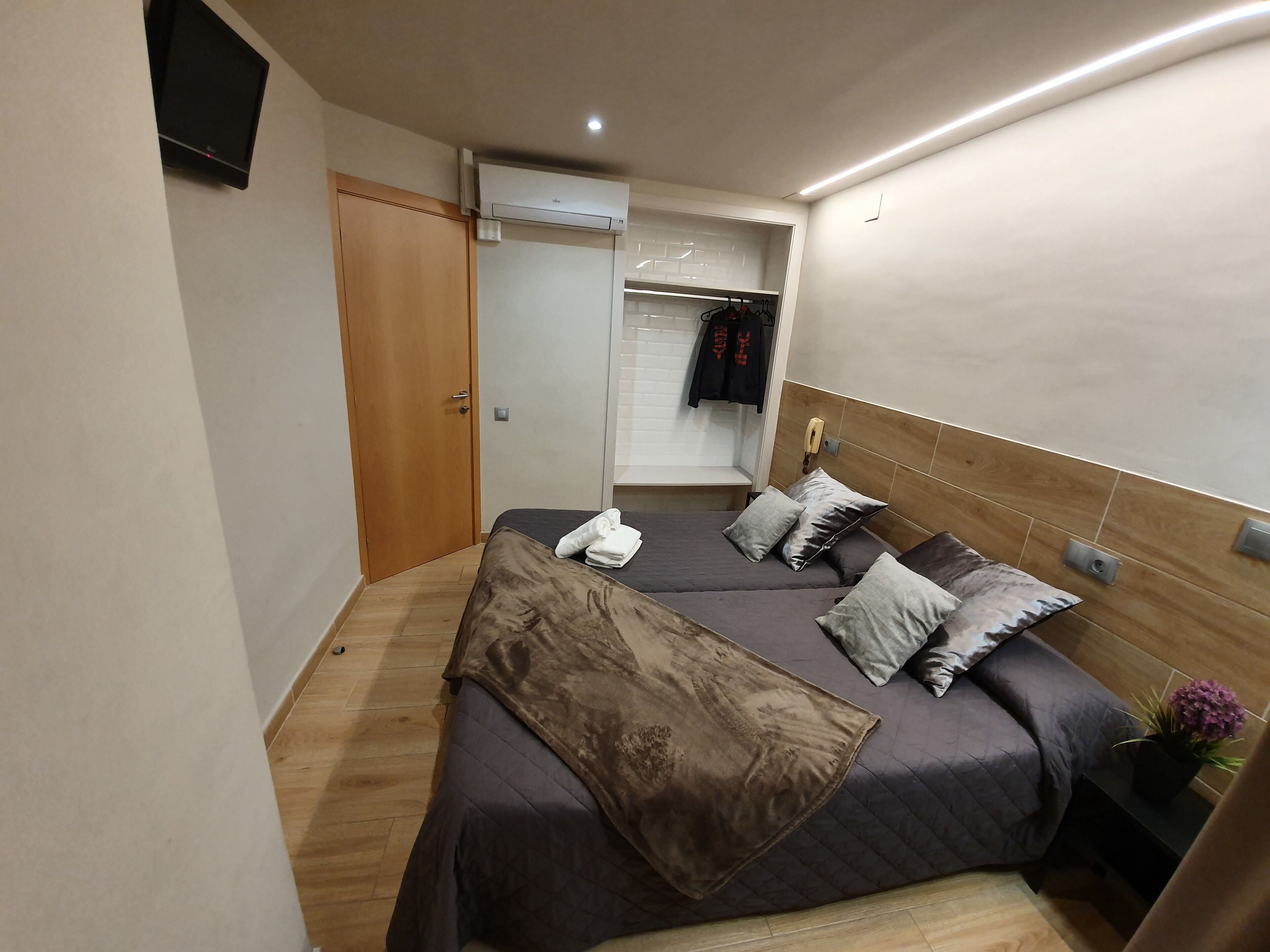 A bedroom with two beds, a wardrobe, a mirror, and a small bedside table with a plant.