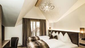 A hotel room with a large bed, a desk, a chair, and a chandelier.